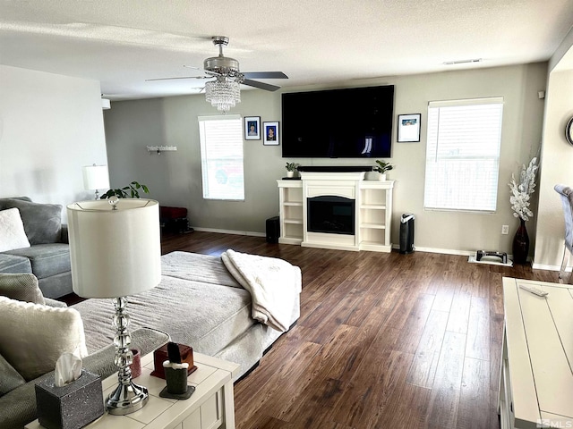 living area featuring baseboards, visible vents, ceiling fan, dark wood-type flooring, and a textured ceiling