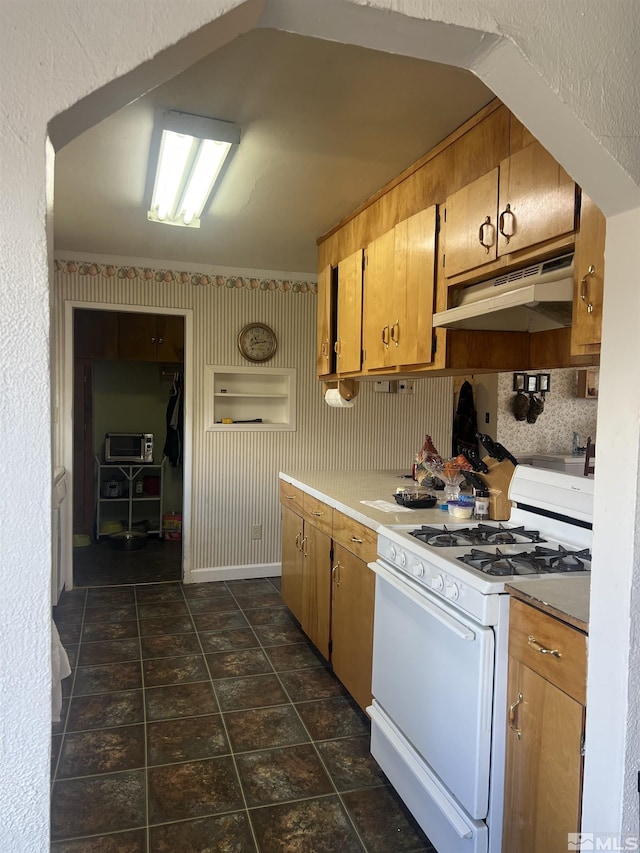 kitchen featuring under cabinet range hood, brown cabinets, baseboards, and gas range gas stove