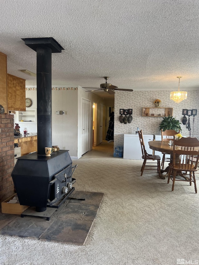 living area featuring a textured ceiling, a wood stove, a ceiling fan, and carpet floors