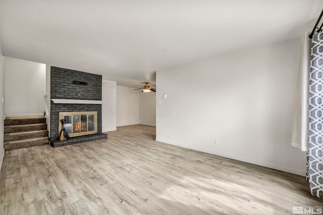 unfurnished living room with a ceiling fan, wood finished floors, a fireplace, baseboards, and stairs