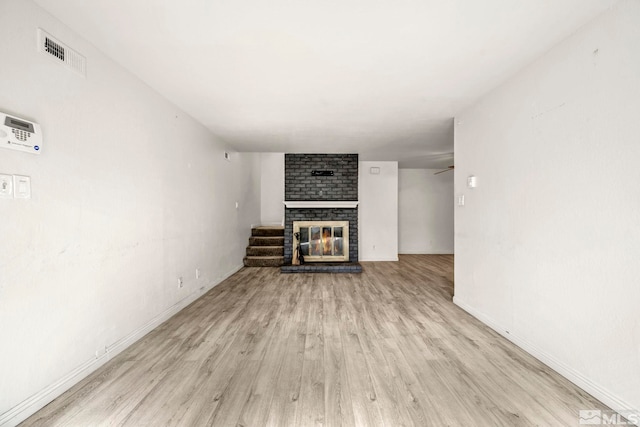 unfurnished living room featuring visible vents, baseboards, a brick fireplace, and light wood-style flooring