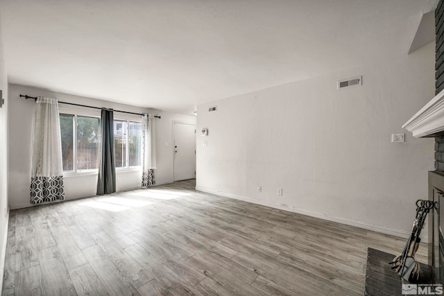 unfurnished living room with visible vents, a fireplace, baseboards, and wood finished floors