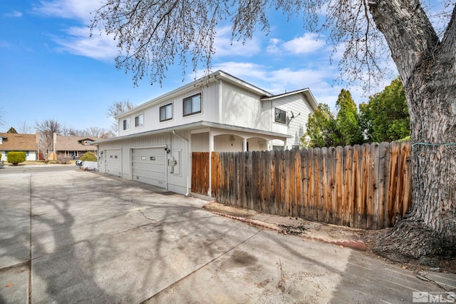 view of side of property with driveway, an attached garage, and fence