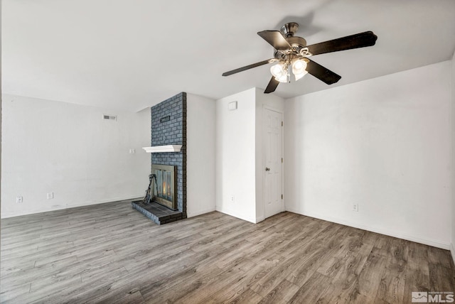 unfurnished living room with a ceiling fan, wood finished floors, visible vents, baseboards, and a brick fireplace