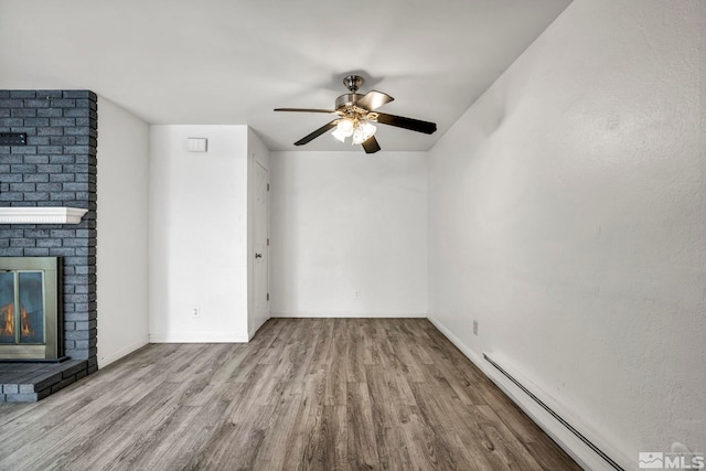 unfurnished living room with wood finished floors, baseboards, ceiling fan, a baseboard heating unit, and a brick fireplace