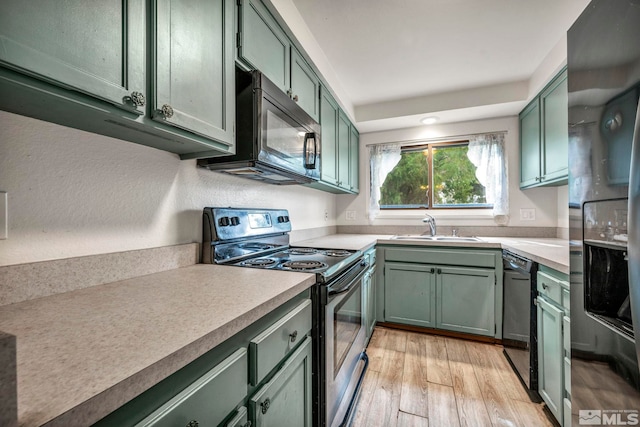 kitchen featuring a sink, light wood-style floors, black appliances, and green cabinets