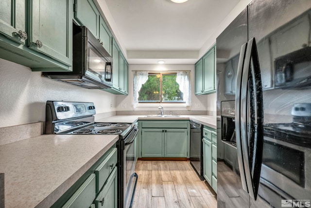 kitchen featuring a sink, black appliances, light wood-style floors, and green cabinetry