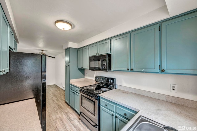 kitchen featuring light wood finished floors, black appliances, light countertops, and a sink