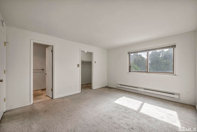 unfurnished bedroom featuring baseboards, carpet floors, ensuite bathroom, a baseboard heating unit, and a walk in closet