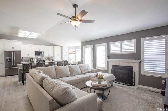 living area featuring vaulted ceiling, a fireplace, light wood-style floors, and ceiling fan