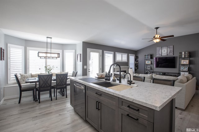 kitchen featuring light wood-type flooring, a center island with sink, a sink, decorative light fixtures, and dishwasher