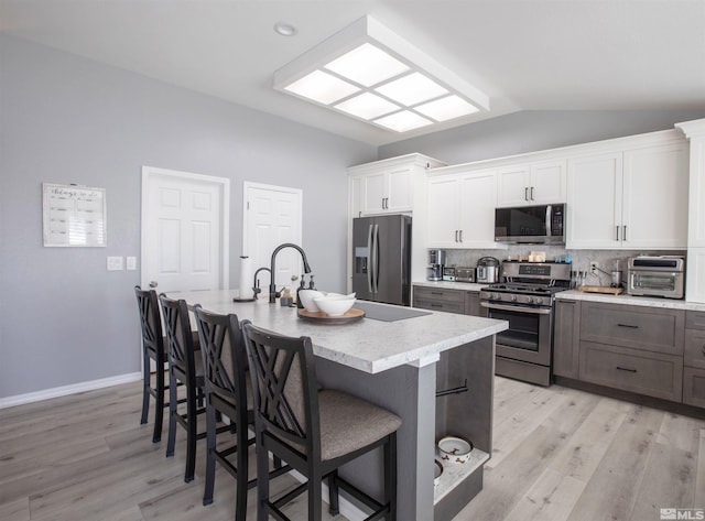 kitchen with stainless steel appliances, a breakfast bar area, white cabinets, decorative backsplash, and vaulted ceiling