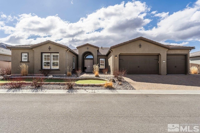 mediterranean / spanish-style home with decorative driveway, a tiled roof, an attached garage, and stucco siding