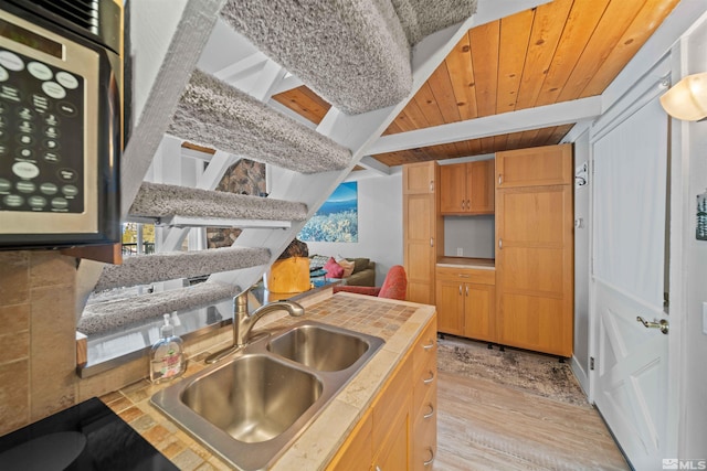 kitchen with beamed ceiling, light wood-style flooring, wooden ceiling, and a sink