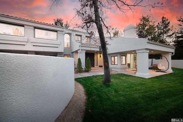 view of front of house with stucco siding, a chimney, a front lawn, and a patio area