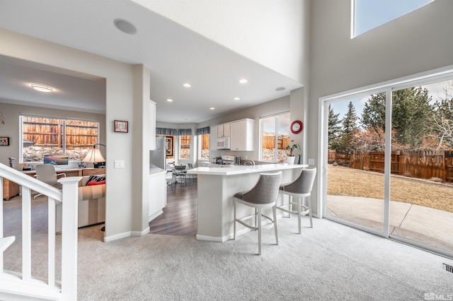 kitchen featuring white microwave, light countertops, white cabinets, a kitchen bar, and light colored carpet