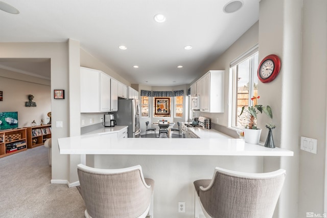 kitchen with white microwave, freestanding refrigerator, light countertops, white cabinets, and light carpet