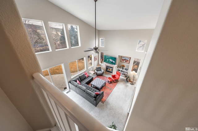 carpeted living room featuring a glass covered fireplace, plenty of natural light, high vaulted ceiling, and a ceiling fan