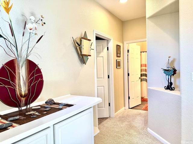 hallway featuring light carpet and baseboards