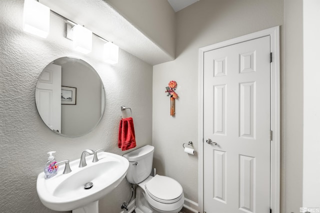 bathroom featuring toilet, a textured wall, and a sink