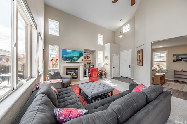 living area featuring a glass covered fireplace, wood finished floors, baseboards, and ceiling fan