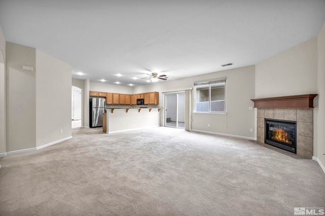 unfurnished living room with a tiled fireplace, visible vents, light carpet, and baseboards