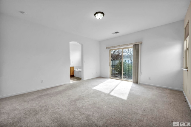 carpeted spare room featuring visible vents, arched walkways, and baseboards