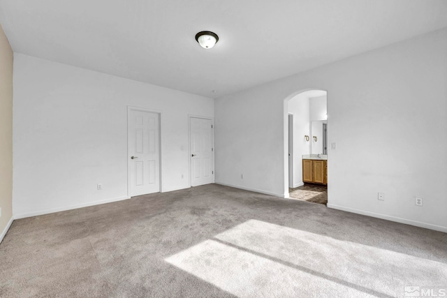 unfurnished bedroom featuring baseboards, arched walkways, carpet, and ensuite bath