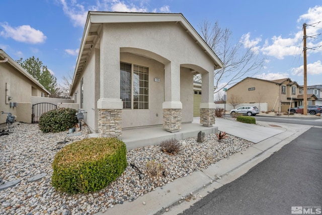 view of front facade with stucco siding, stone siding, driveway, and a gate