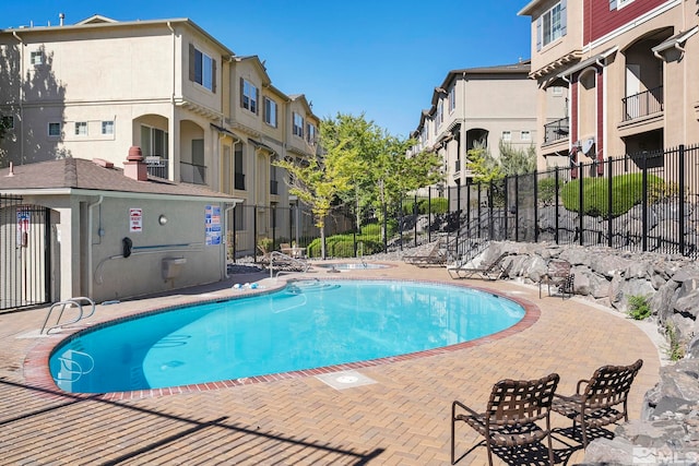 community pool with a patio, fence, and a residential view