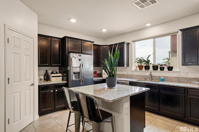 kitchen featuring visible vents, light stone countertops, a breakfast bar area, stainless steel refrigerator with ice dispenser, and a sink