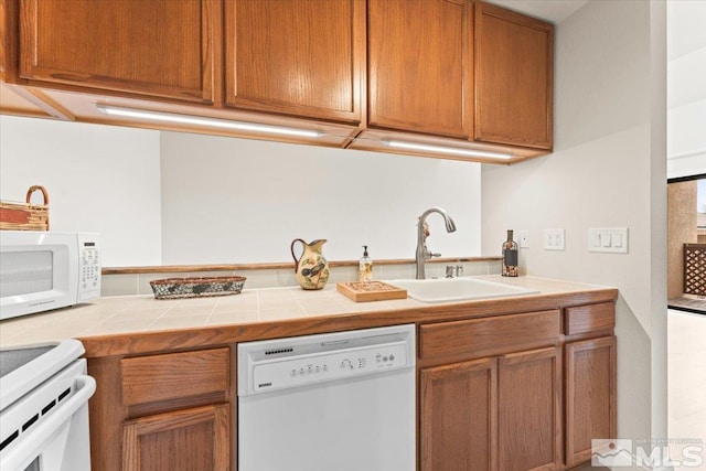 kitchen with a sink, white appliances, tile countertops, and brown cabinetry