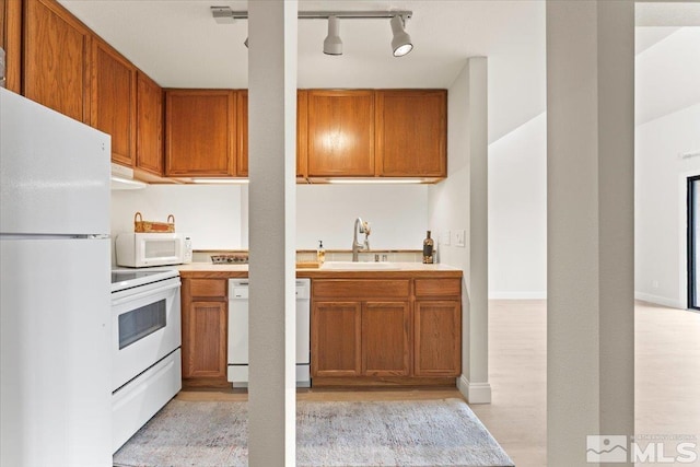 kitchen featuring light wood finished floors, light countertops, brown cabinetry, white appliances, and a sink