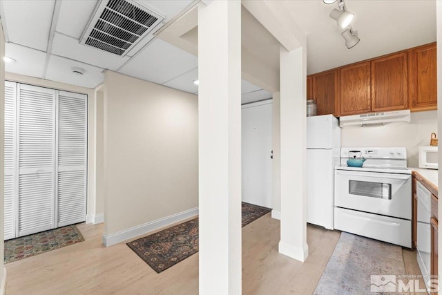 kitchen with visible vents, under cabinet range hood, light wood-style flooring, brown cabinetry, and white appliances