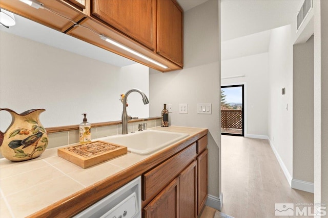 kitchen featuring baseboards, visible vents, a sink, tile counters, and brown cabinets