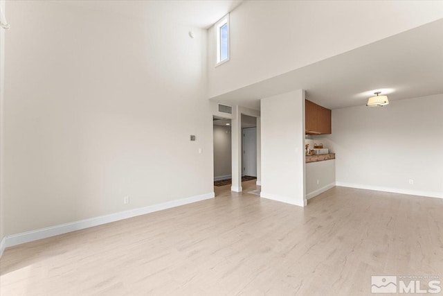 unfurnished living room with visible vents, a high ceiling, light wood-type flooring, and baseboards