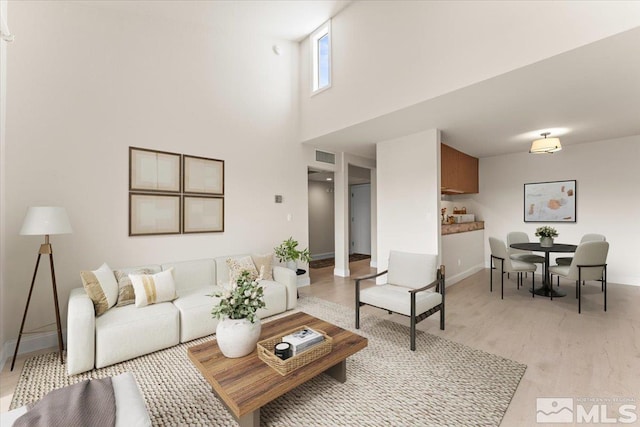 living area featuring light wood-type flooring, baseboards, a high ceiling, and visible vents