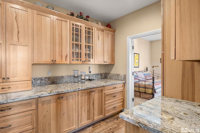 kitchen featuring light stone counters, glass insert cabinets, light brown cabinetry, and light wood finished floors