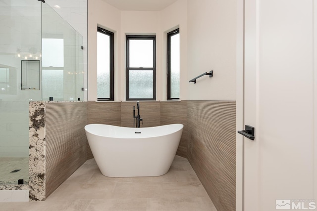 full bathroom featuring wainscoting, a stall shower, tile patterned floors, a soaking tub, and tile walls