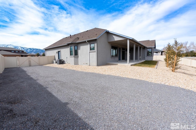 rear view of house with stucco siding, cooling unit, a fenced backyard, a patio area, and a gate