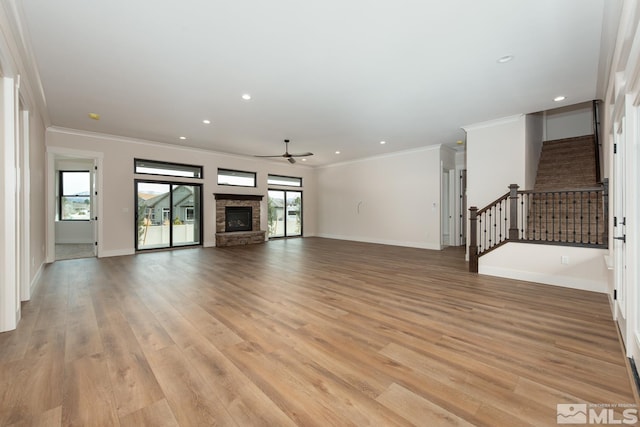 unfurnished living room with ornamental molding, light wood-style floors, a fireplace, baseboards, and stairs