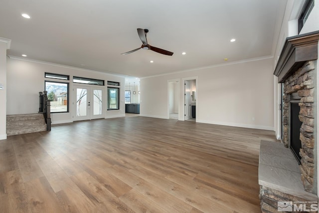 unfurnished living room with light wood finished floors, a stone fireplace, french doors, and ornamental molding