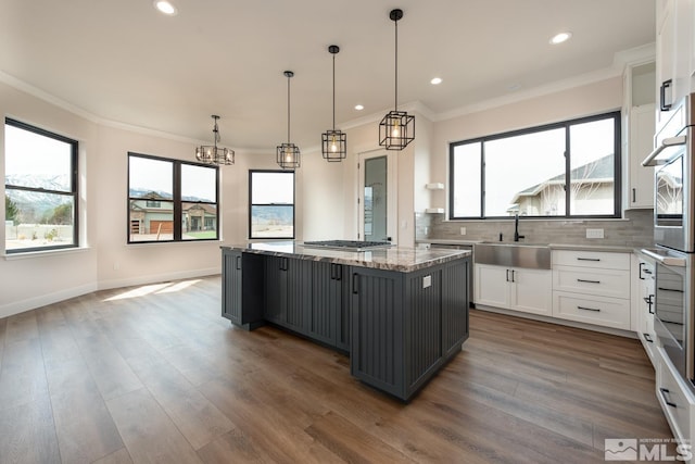 kitchen featuring ornamental molding, a sink, a kitchen island, white cabinets, and decorative backsplash