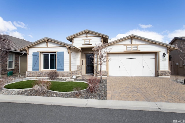 view of front of home featuring decorative driveway, stone siding, an attached garage, and a tiled roof