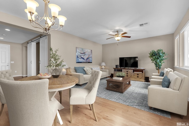 dining space with visible vents, ceiling fan, baseboards, light wood-type flooring, and a barn door