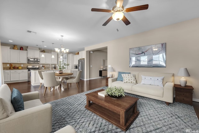 living area featuring visible vents, baseboards, dark wood-style floors, and ceiling fan with notable chandelier