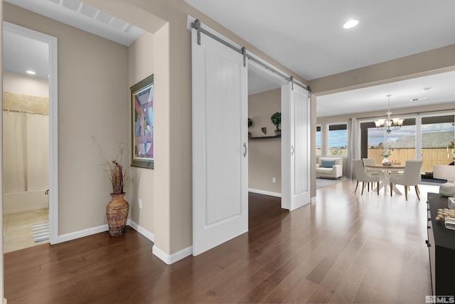 corridor with a barn door, baseboards, dark wood-type flooring, and an inviting chandelier