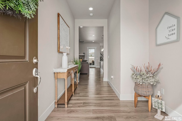 foyer entrance featuring light wood-style flooring, baseboards, and a lit fireplace