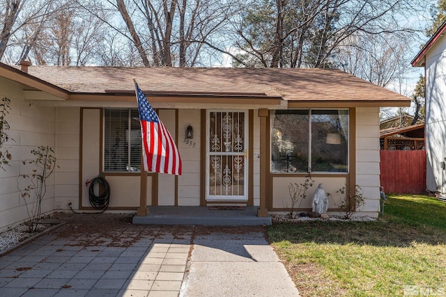 doorway to property with fence, a lawn, and roof with shingles