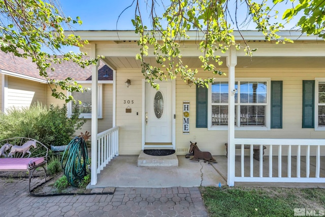 entrance to property with covered porch and a shingled roof